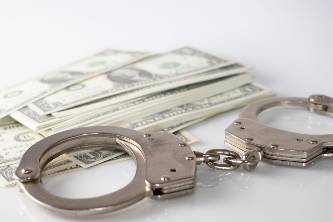 Handcuffs placed beside stacks of U.S. dollar bills symbolizing financial crime and corruption